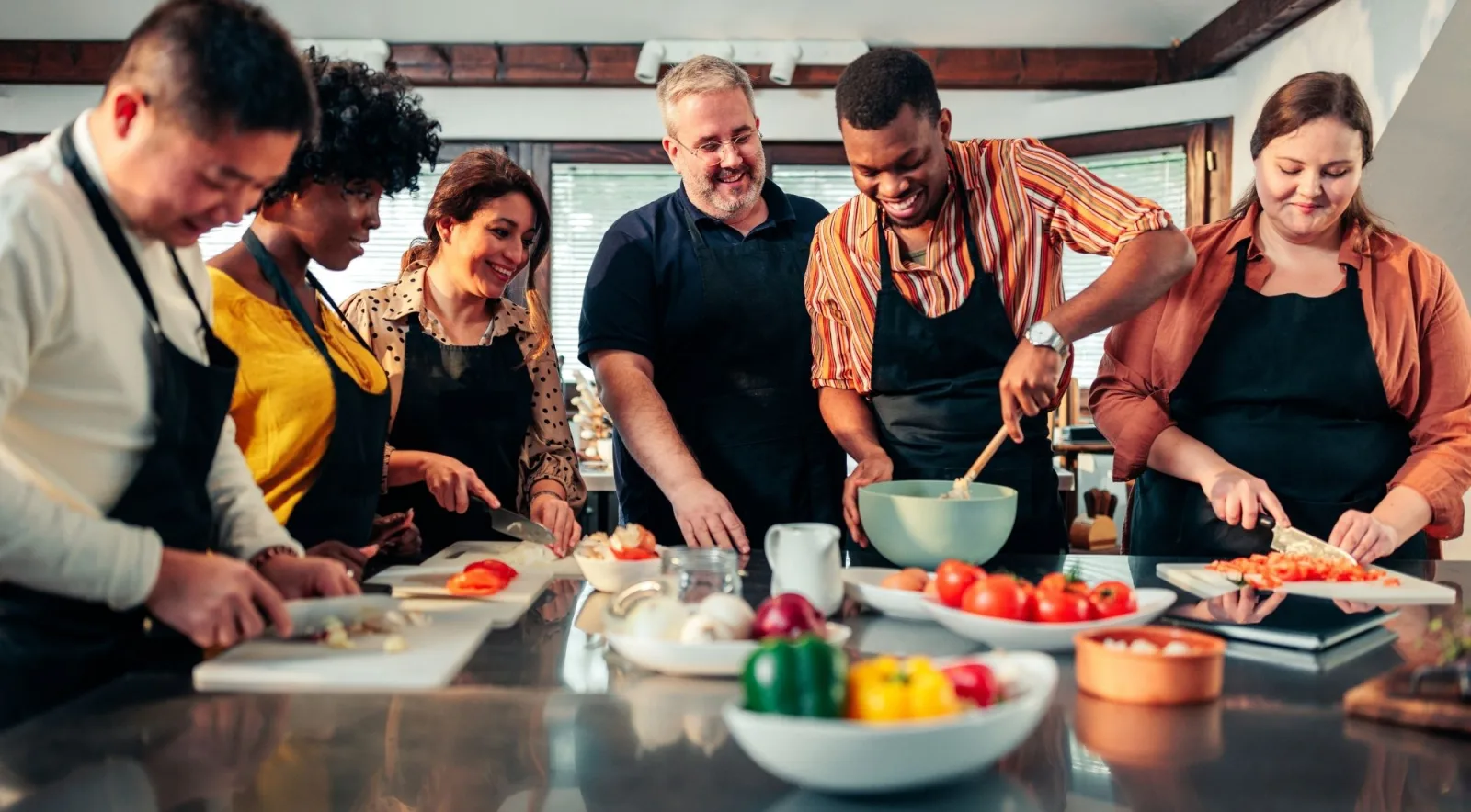 A group of guests in aprons chopping vegetables around a kitchen island during a cooking class