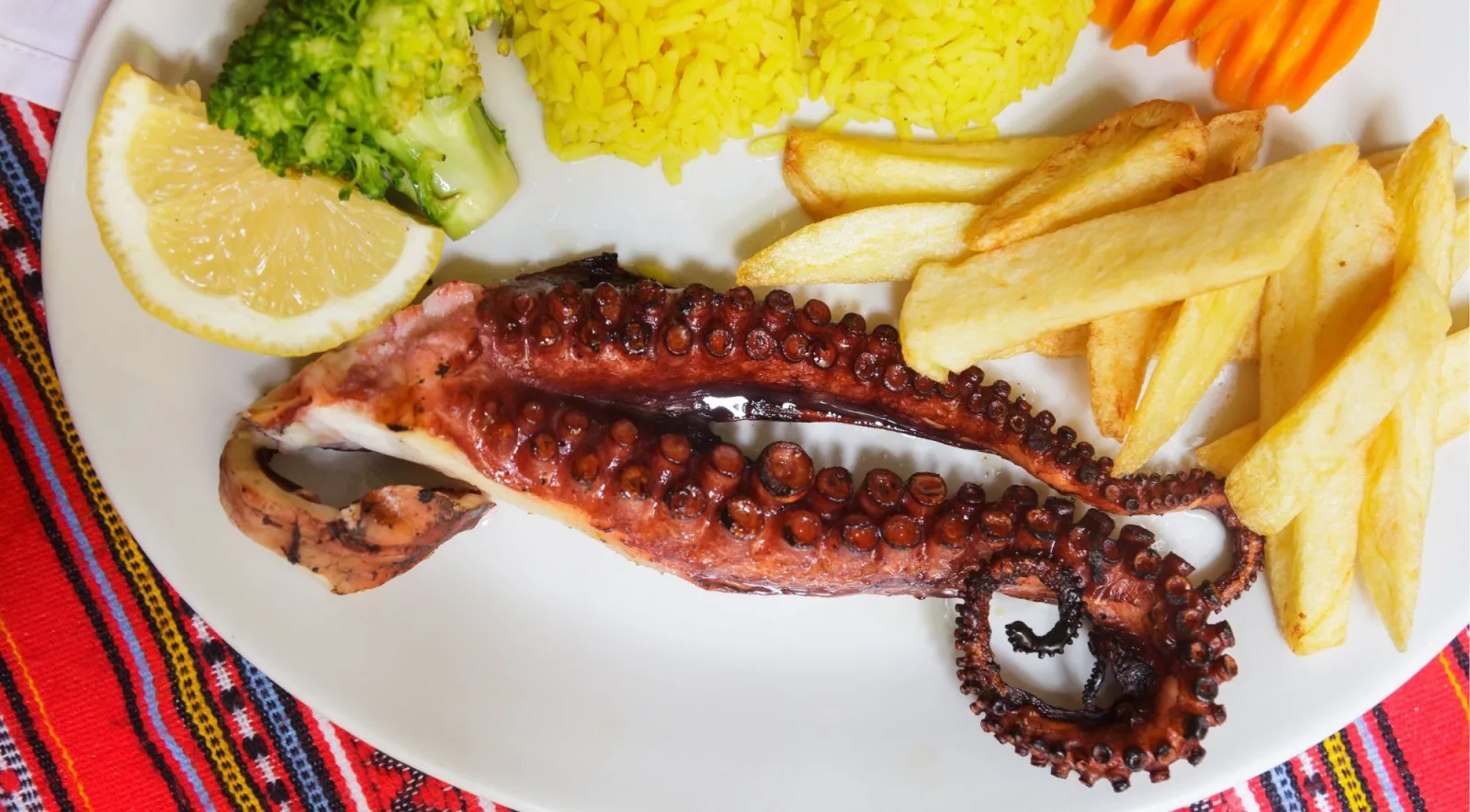 Grilled octopus served with lemon, rice and fried potatoes on a white plate