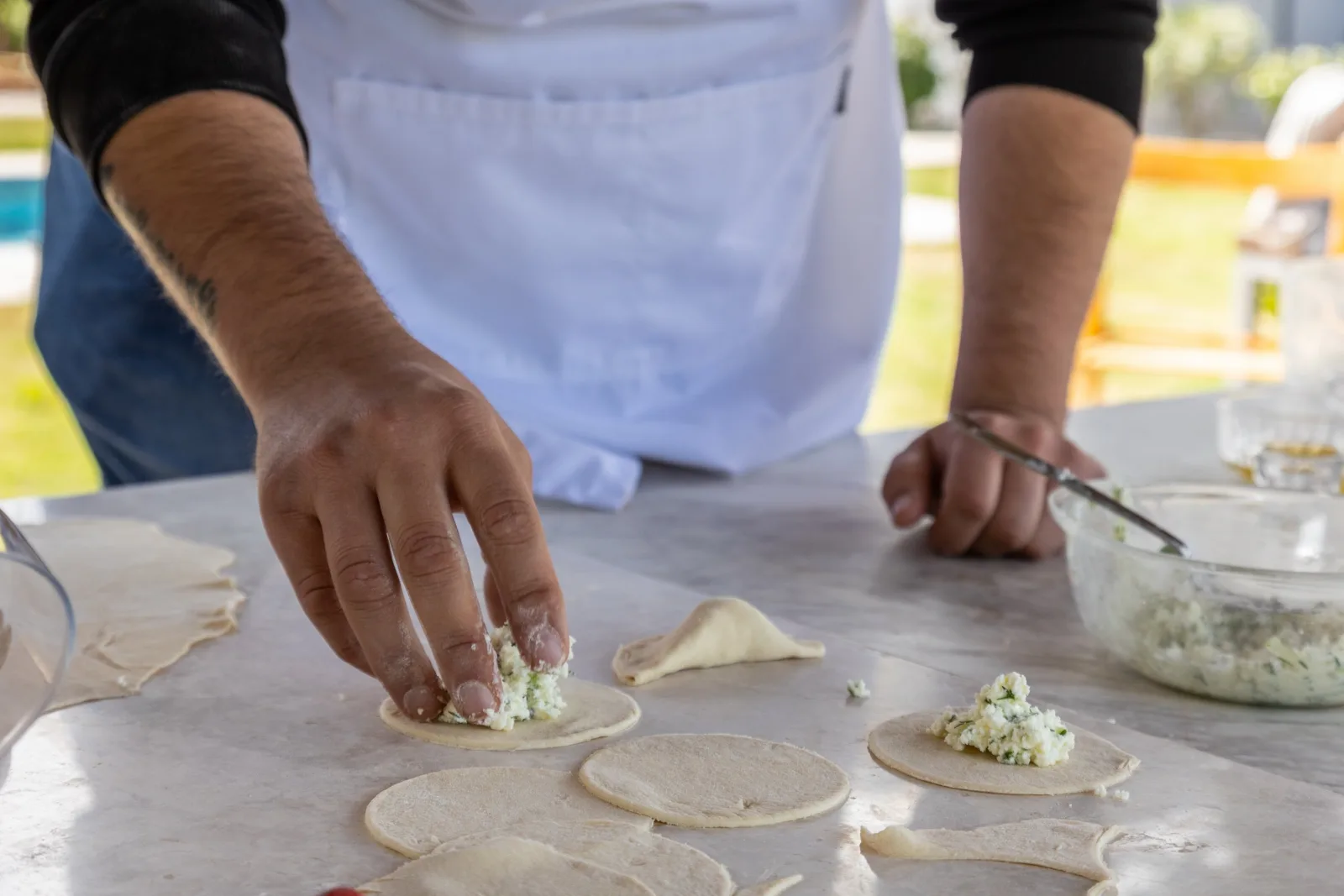 Hands filling and crimping rounds of dough with soft white cheese on a marble worktop