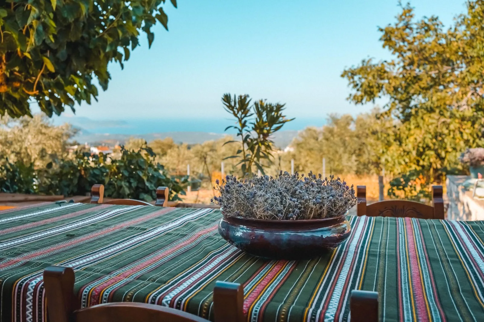 A table laid with a striped Cretan runner on a mountain terrace above Chania, looking out over olive trees to the sea