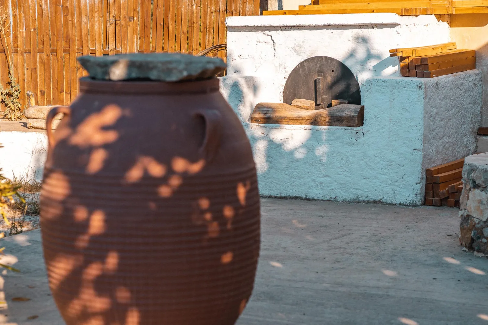 A large terracotta storage pithos standing in front of a whitewashed outdoor wood oven