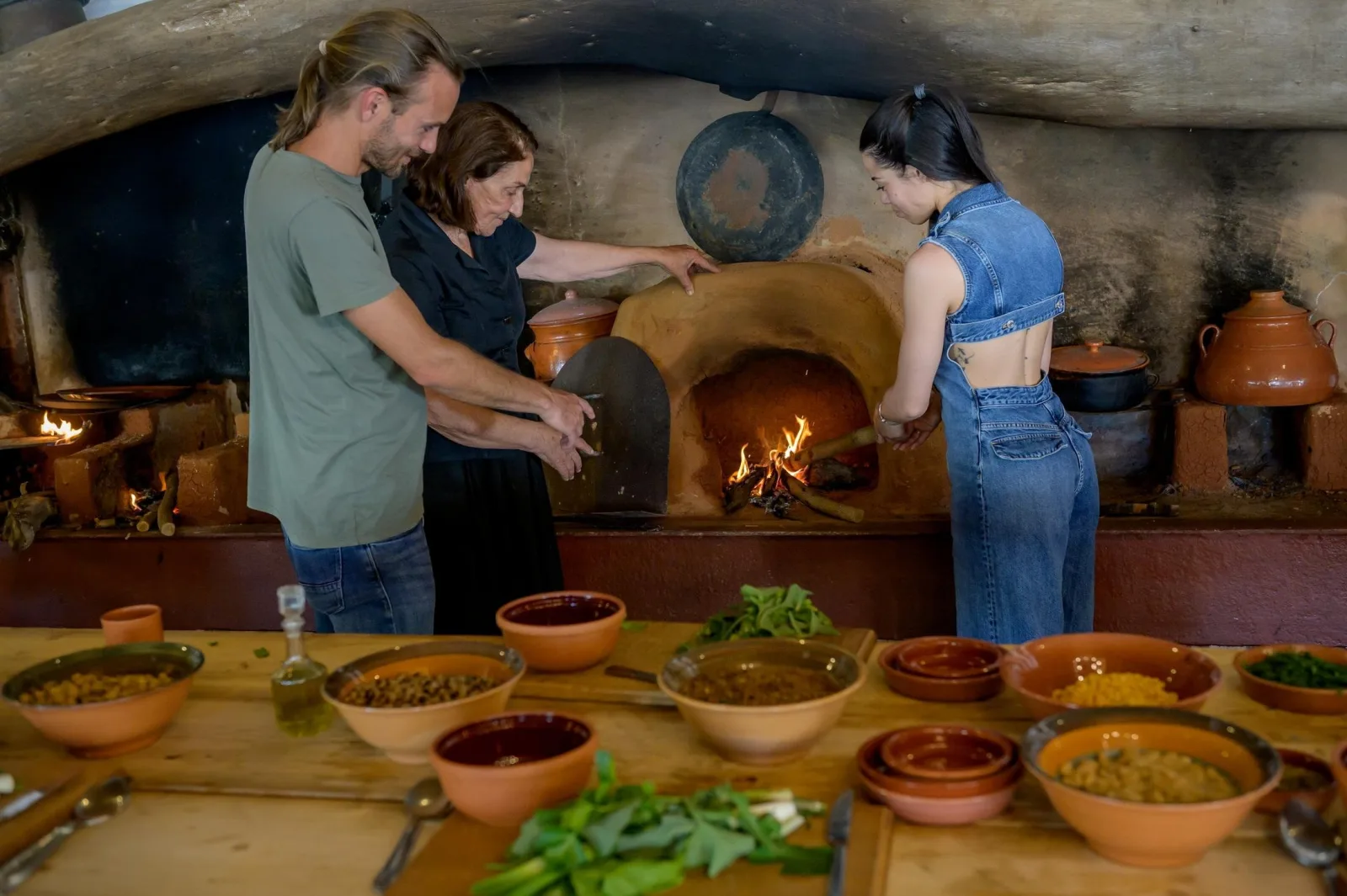 Guests at a lit clay oven with terracotta bowls of ingredients ranged along the bench
