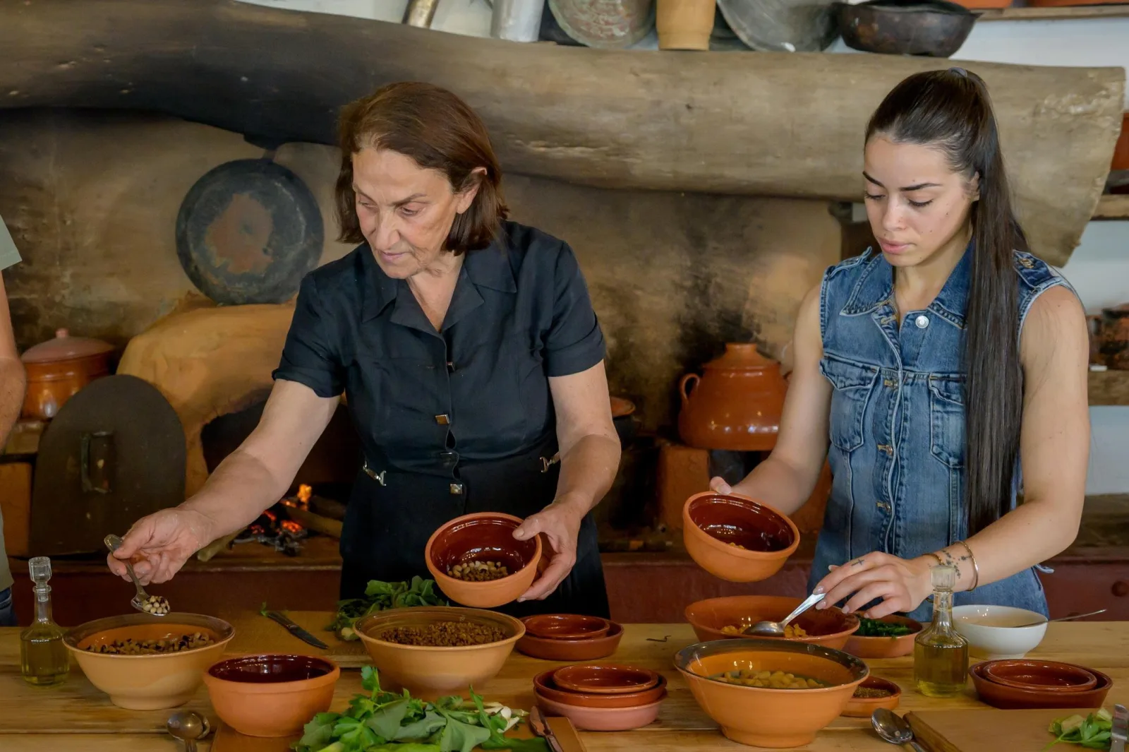 Two guests grinding ingredients in clay ware beside the domed Minoan oven