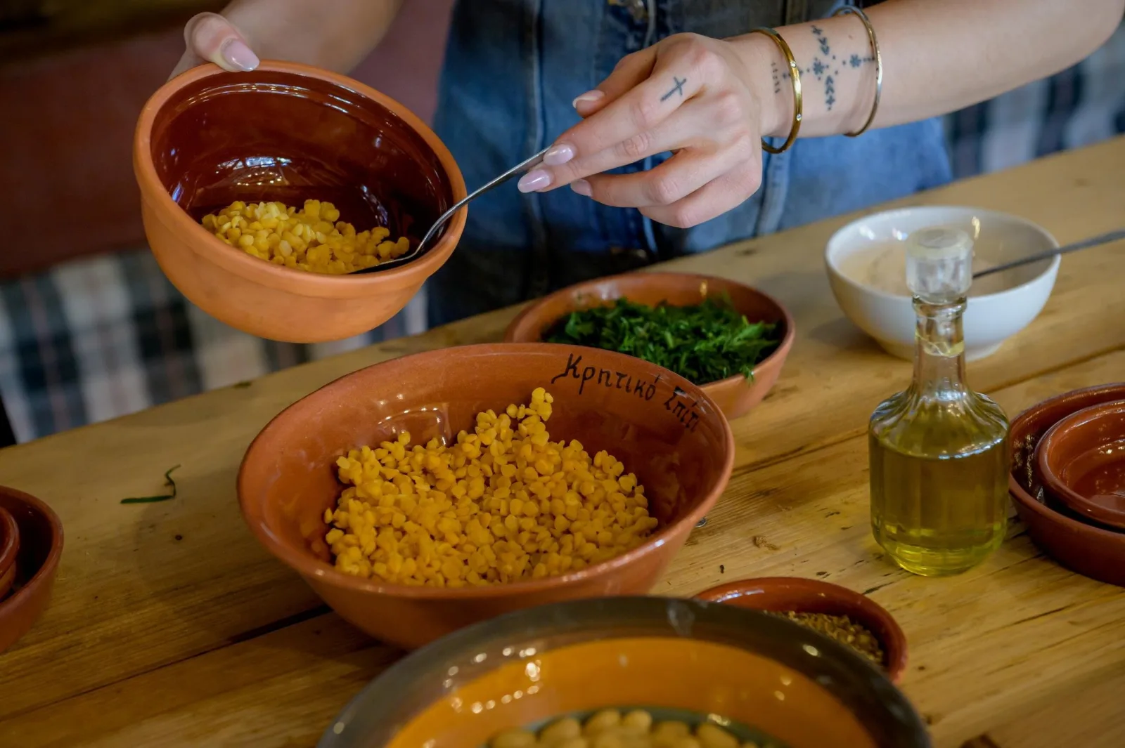 A hand spooning yellow split peas into a terracotta bowl beside a jug of olive oil