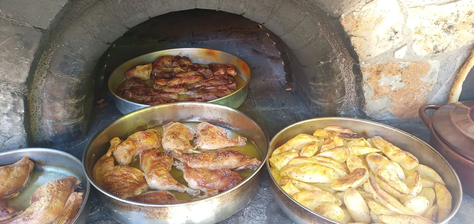 Trays of roast chicken, potatoes and pies baking inside a wood-fired oven