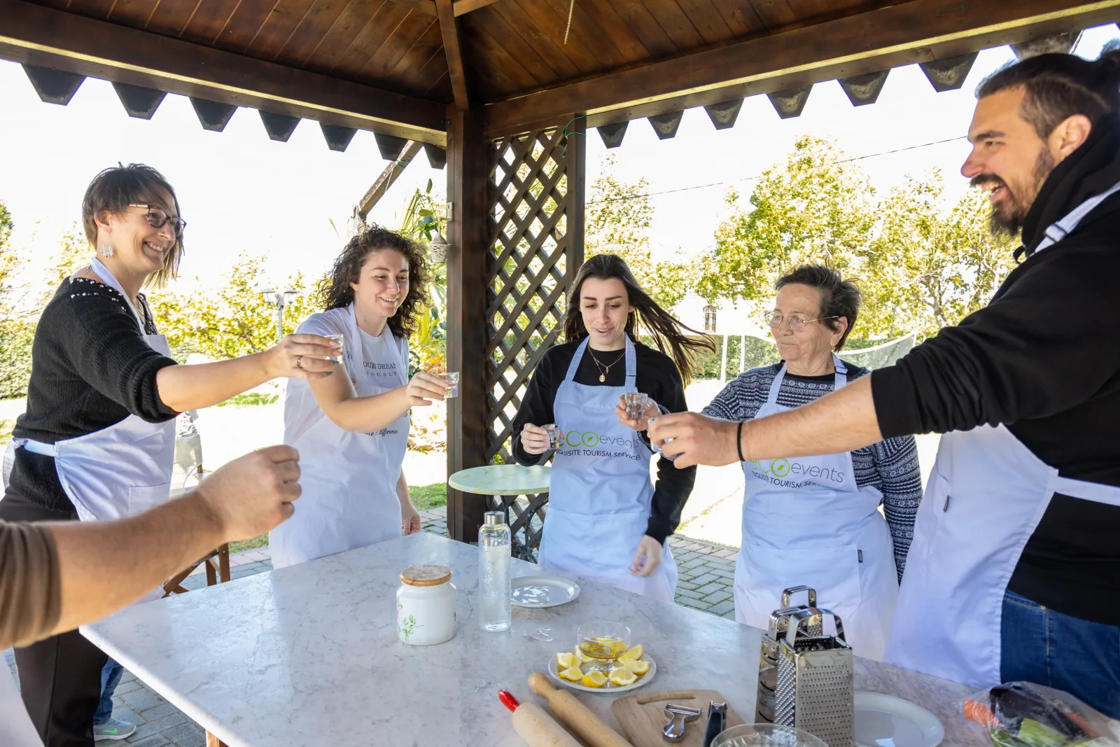 Guests in aprons raising their glasses around a steel prep table in the garden gazebo