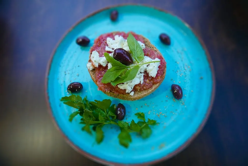 A plate of dakos topped with tomato, crumbled cheese and olives