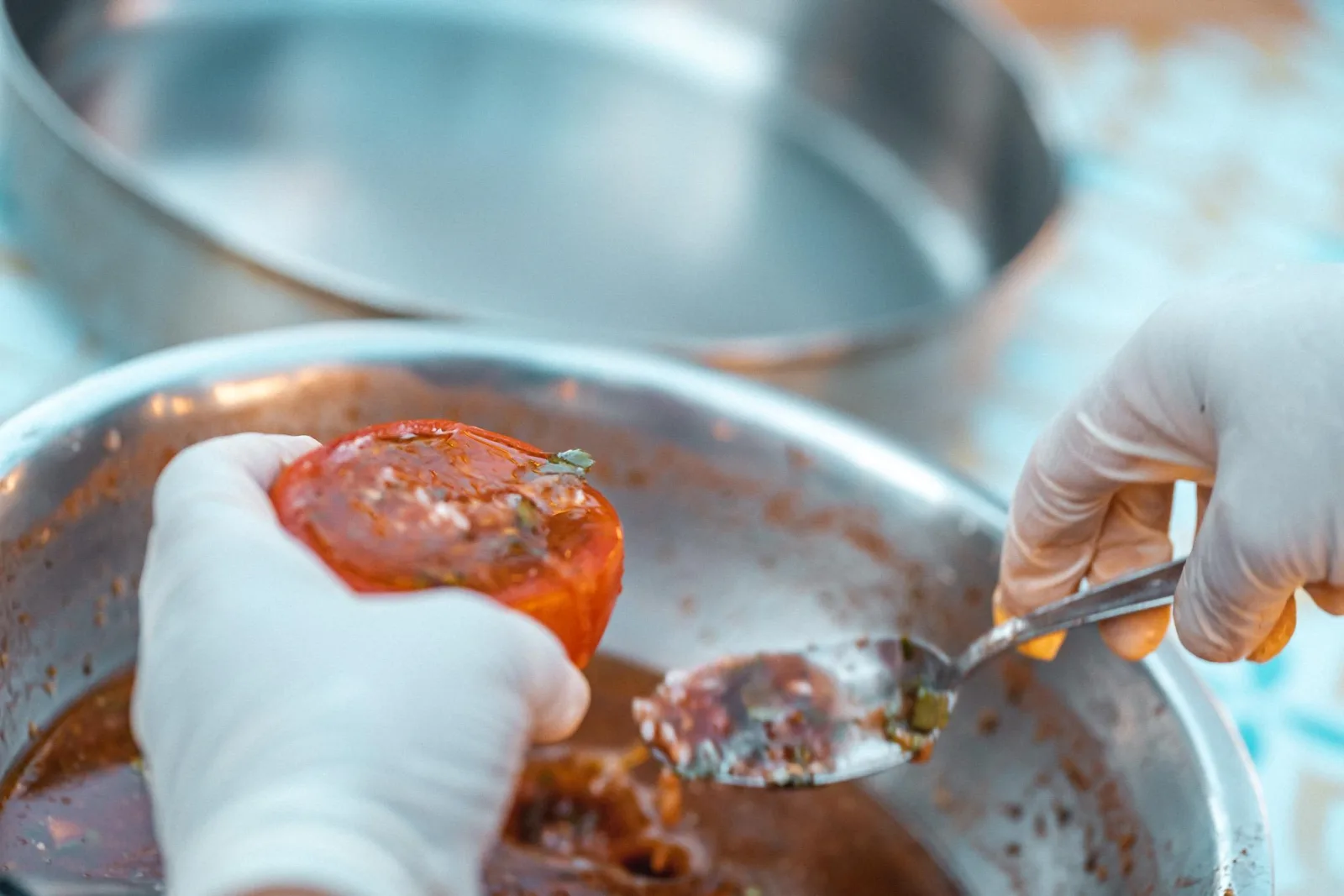 A gloved hand lifting tomato sauce from a large cooking pot with a ladle